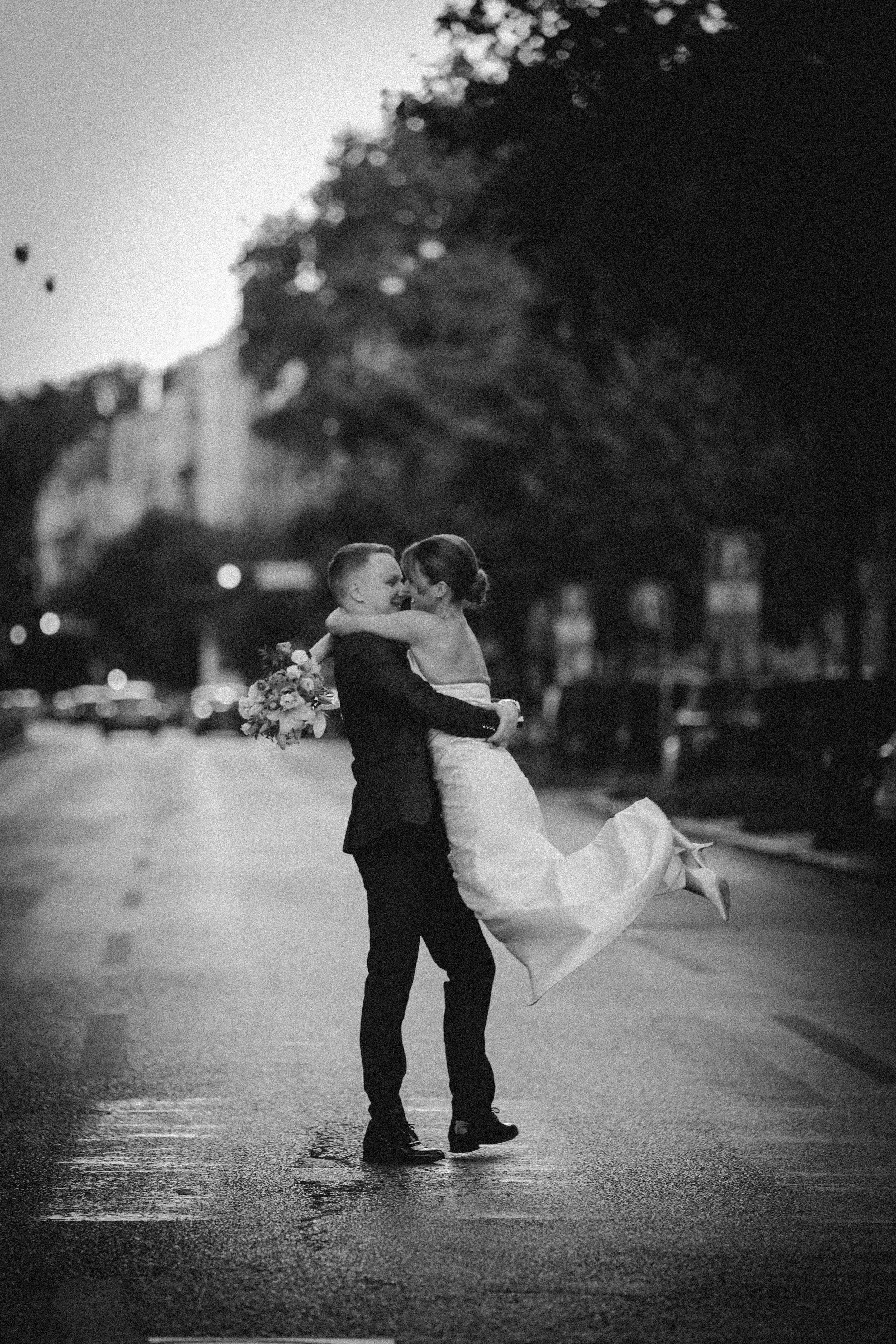 Romantic black and white dance pose on a rainy city street with flowing wedding dress.