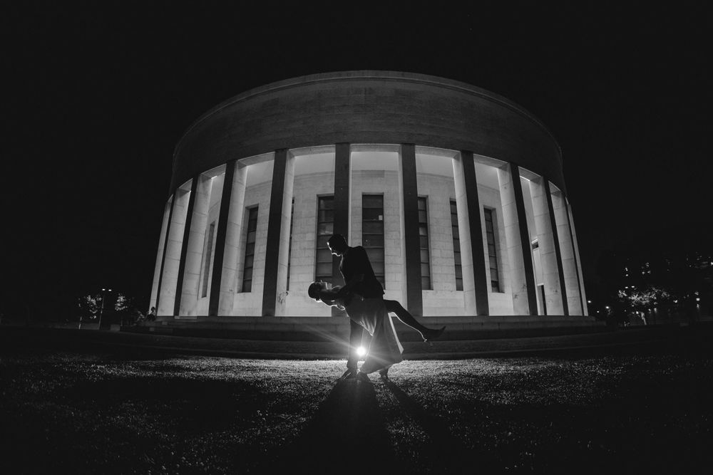 Dramatic nighttime silhouette of a wedding couple in front of an illuminated circular building.