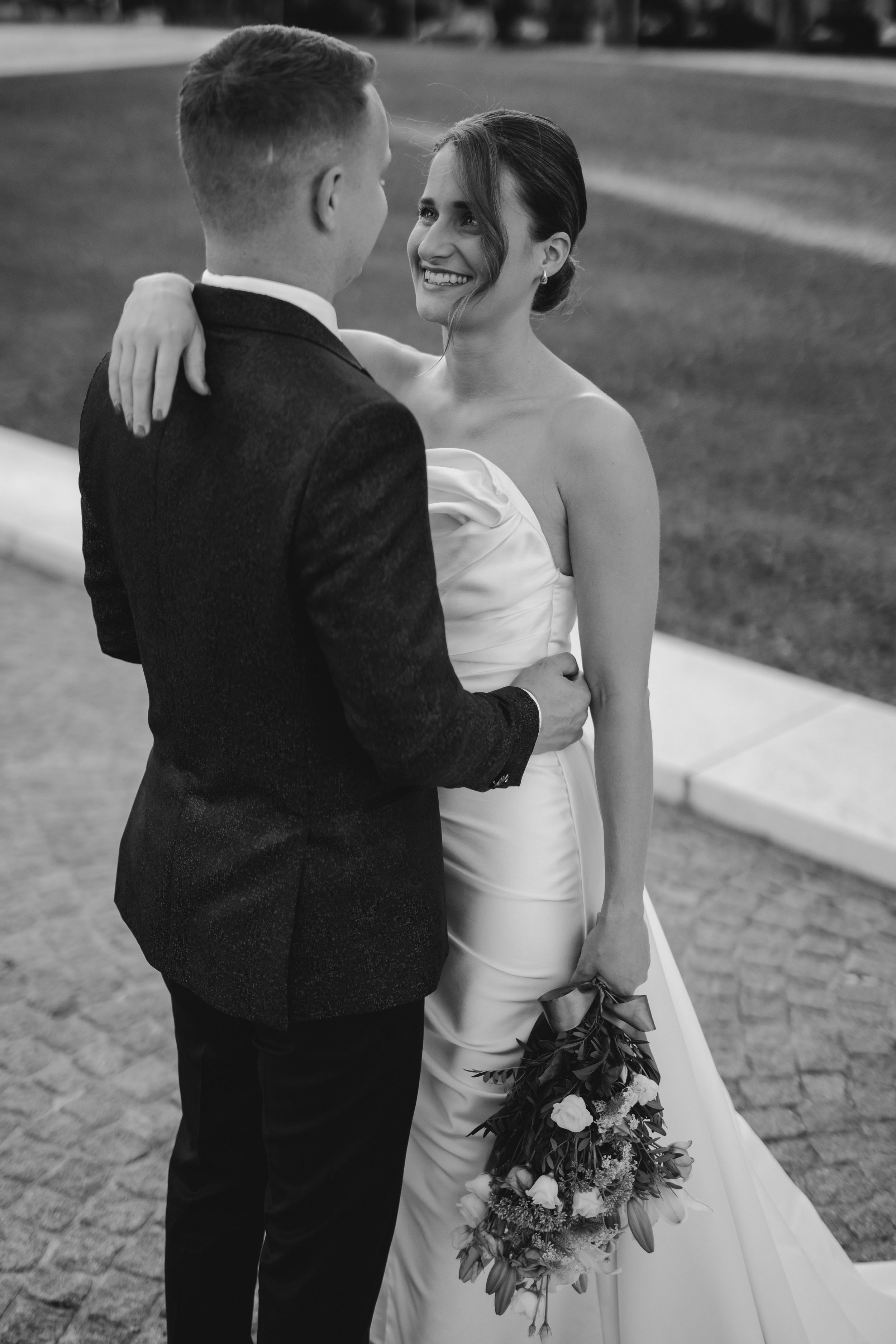 Black and white portrait of newlyweds sharing an intimate moment with bride holding bouquet.