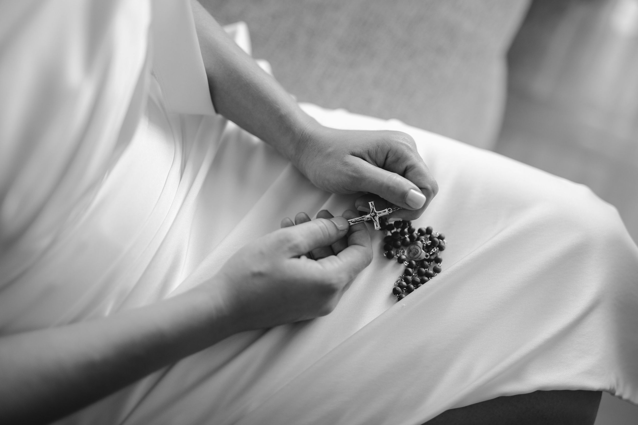 Close-up black and white detail of hands adjusting jewelry on a white wedding dress.