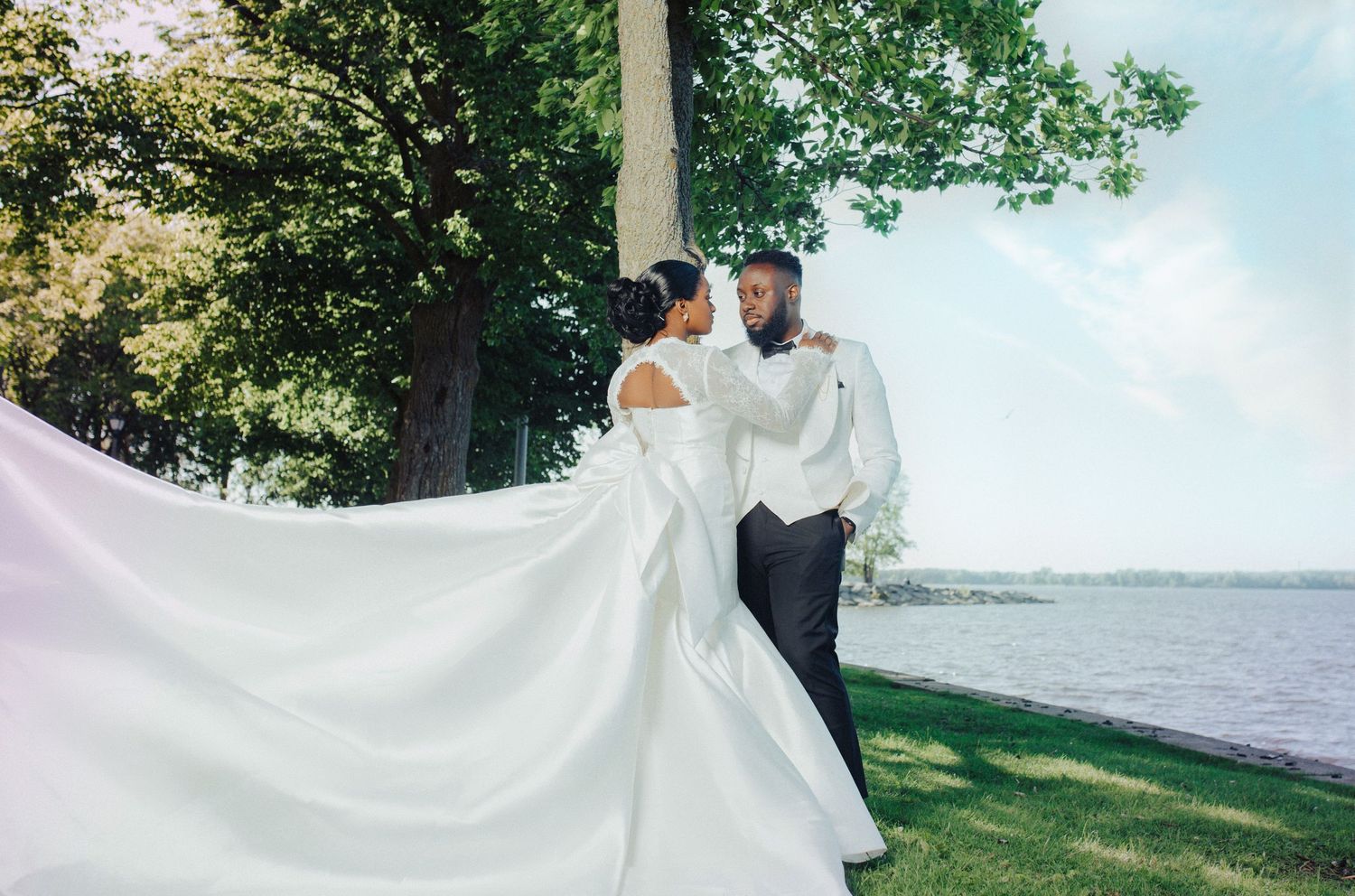 A romantic wedding photo by the water with a flowing white dress billowing in the breeze on a sunny summer day.