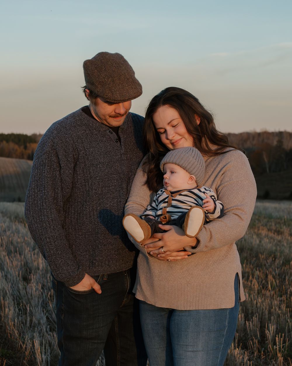 A family shares an intimate moment together in a field at sunset wearing cozy sweaters.