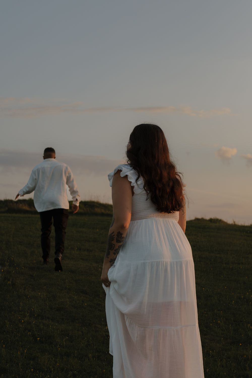 A romantic sunset scene with a couple walking through a grassy meadow in wedding attire.