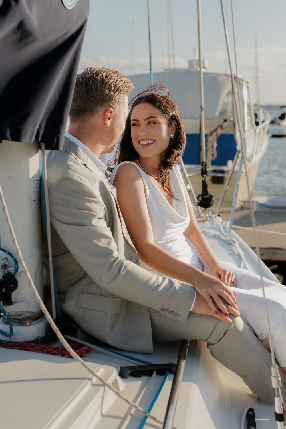 A romantic couple in wedding attire share an intimate moment while sitting on a sailboat under blue skies.