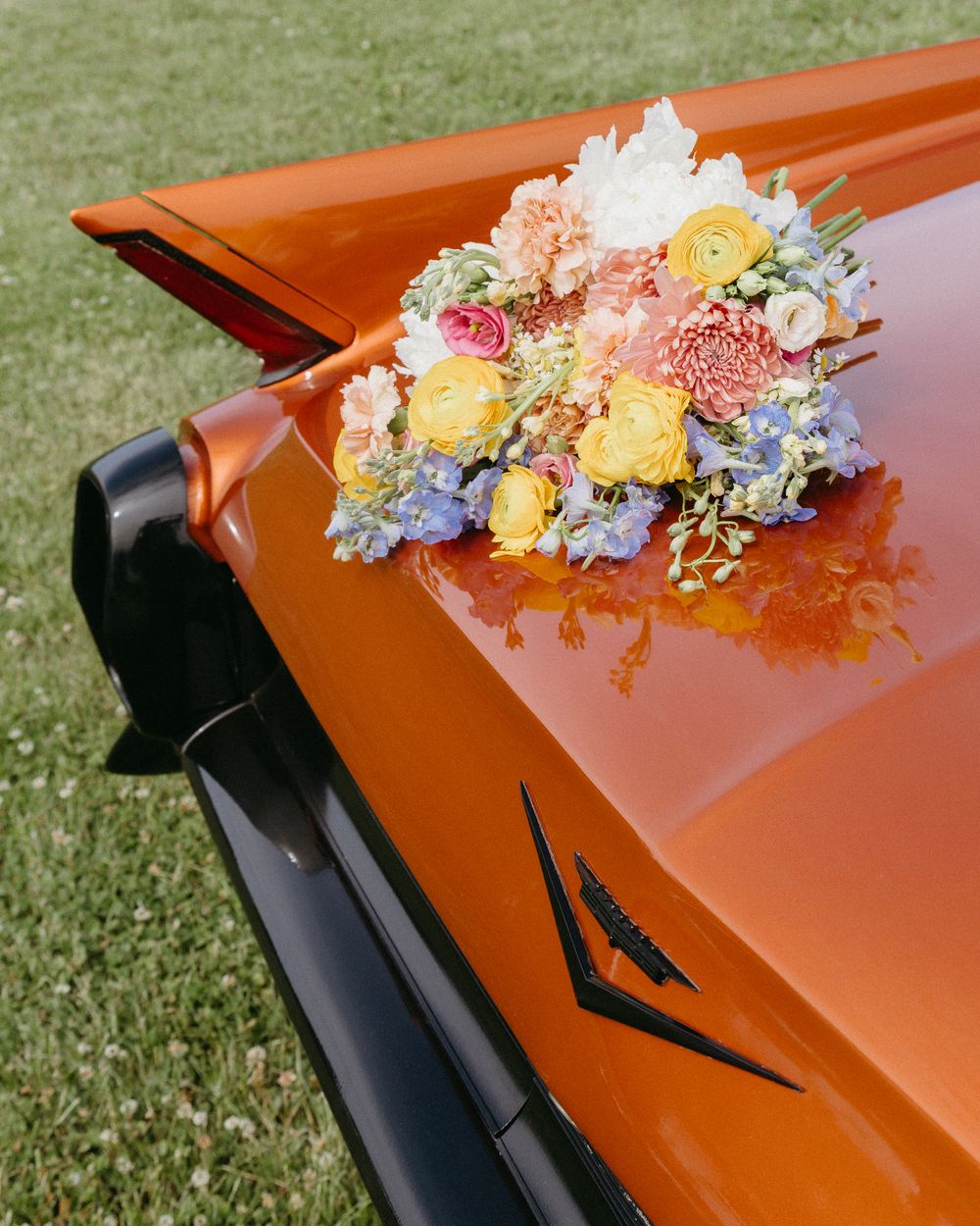 Colorful floral arrangement with yellow and pink flowers decorates the corner of an orange surface outdoors on grass.