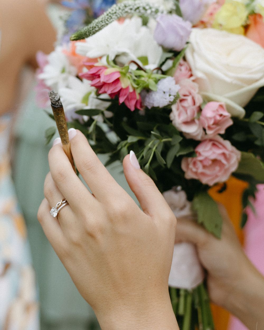 Close-up view of hands holding a delicate bouquet of pink and white flowers with an engagement ring.