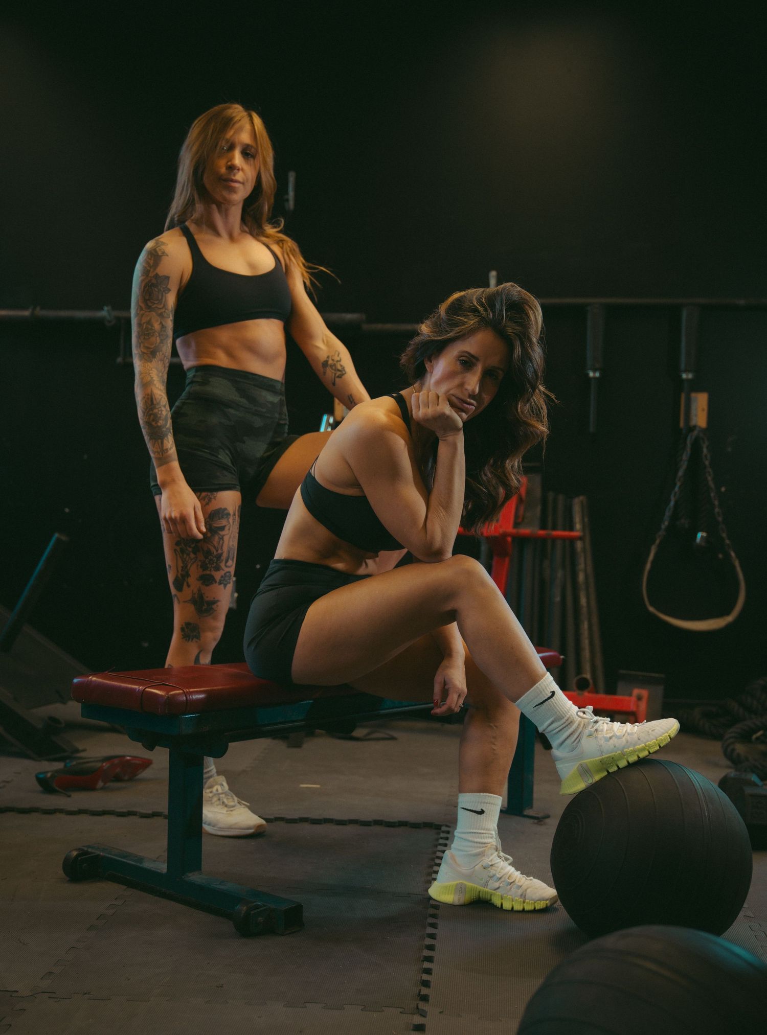 Fitness photography in a dark gym setting featuring exercise equipment and athletic wear.