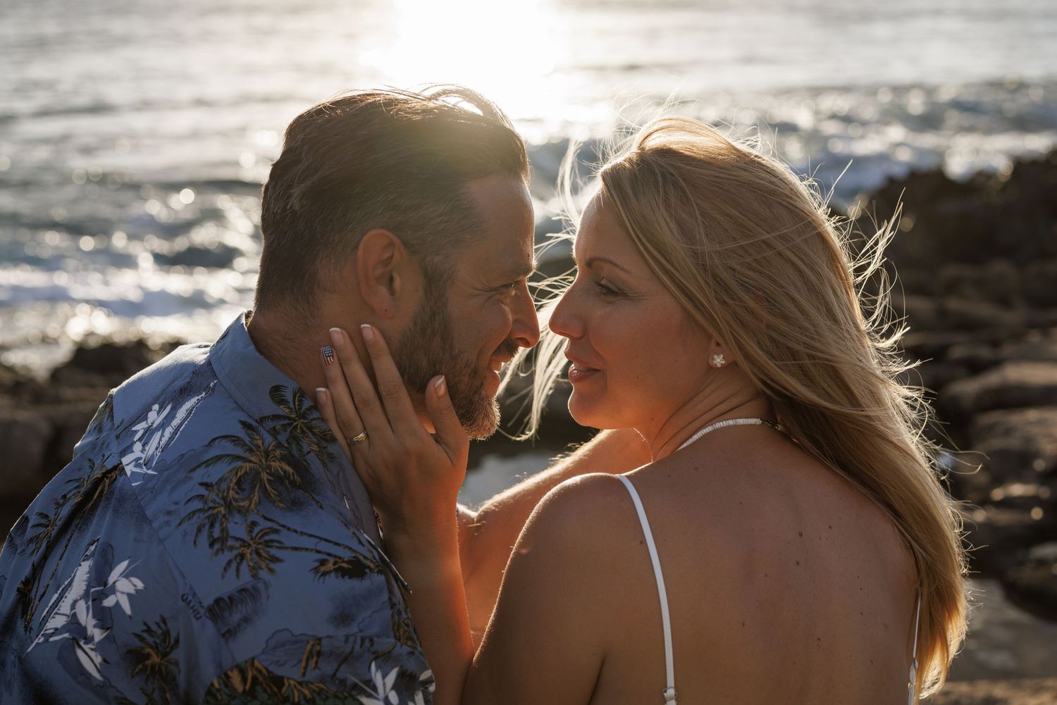 Romantic couple sharing an intimate moment on a rocky beach at sunset, woman touching mans face tenderly.