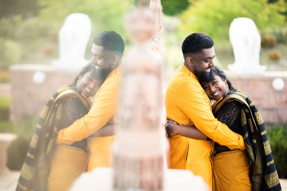 Two people sharing a warm embrace while wearing yellow and green outfits in an outdoor setting with a soft blurred background.
