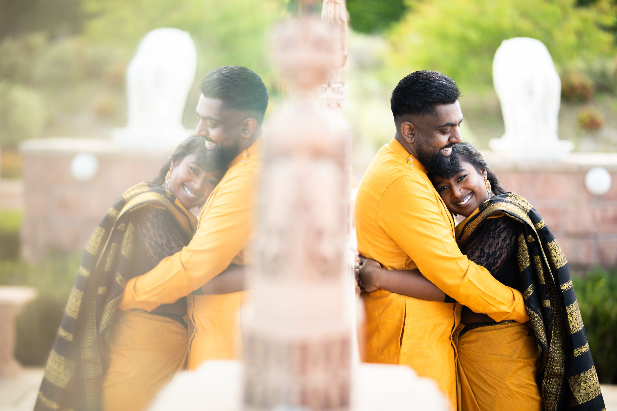 Two people sharing a warm embrace while wearing yellow and green outfits in an outdoor setting with a soft blurred background.