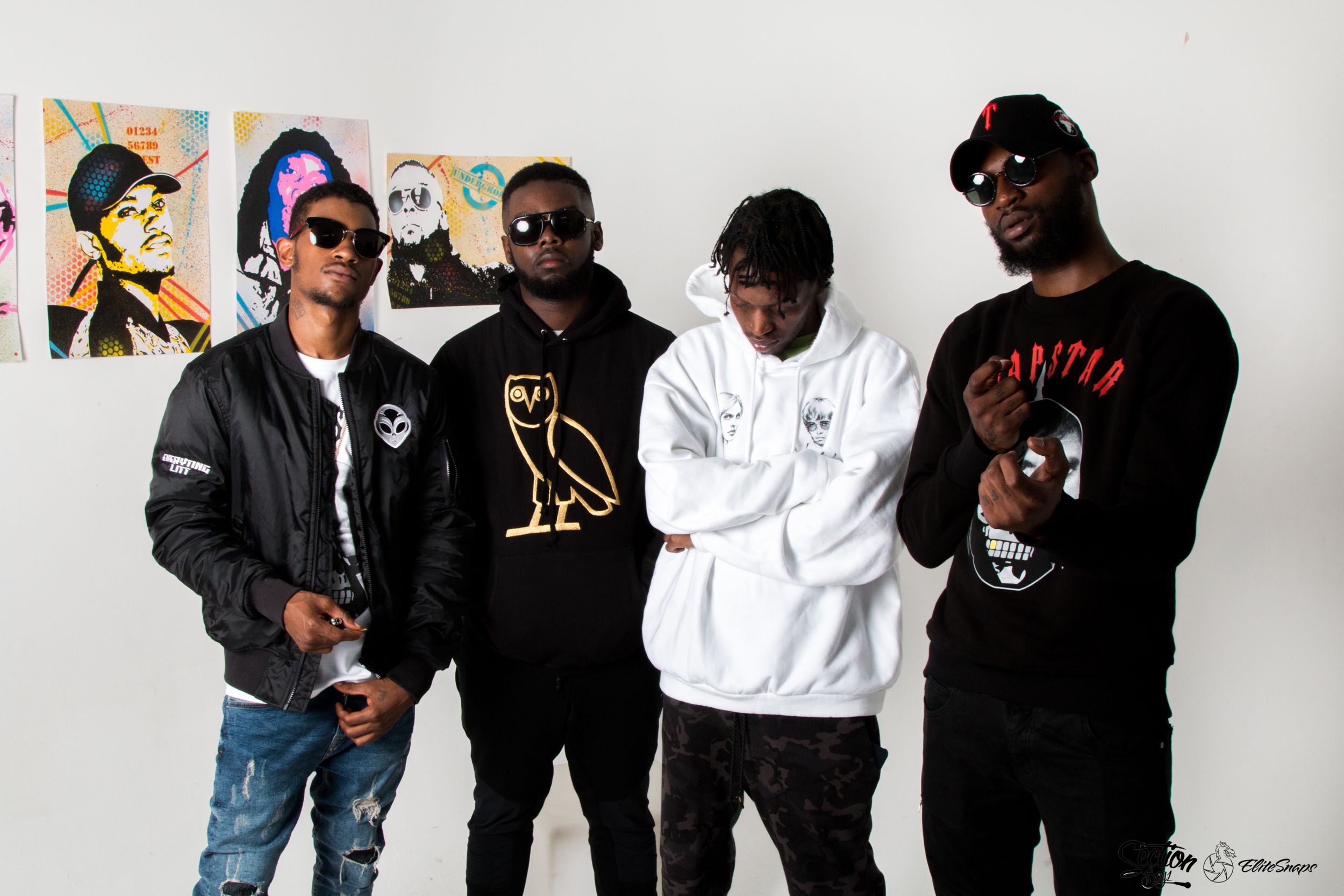A group of four people posing against a white wall wearing casual streetwear and hoodies. Section Boyz