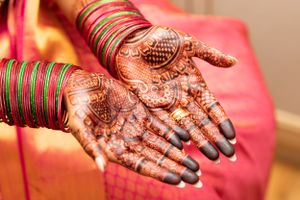 Traditional henna mehndi designs adorning palms with bangles and red fabric in an Indian wedding ceremony.