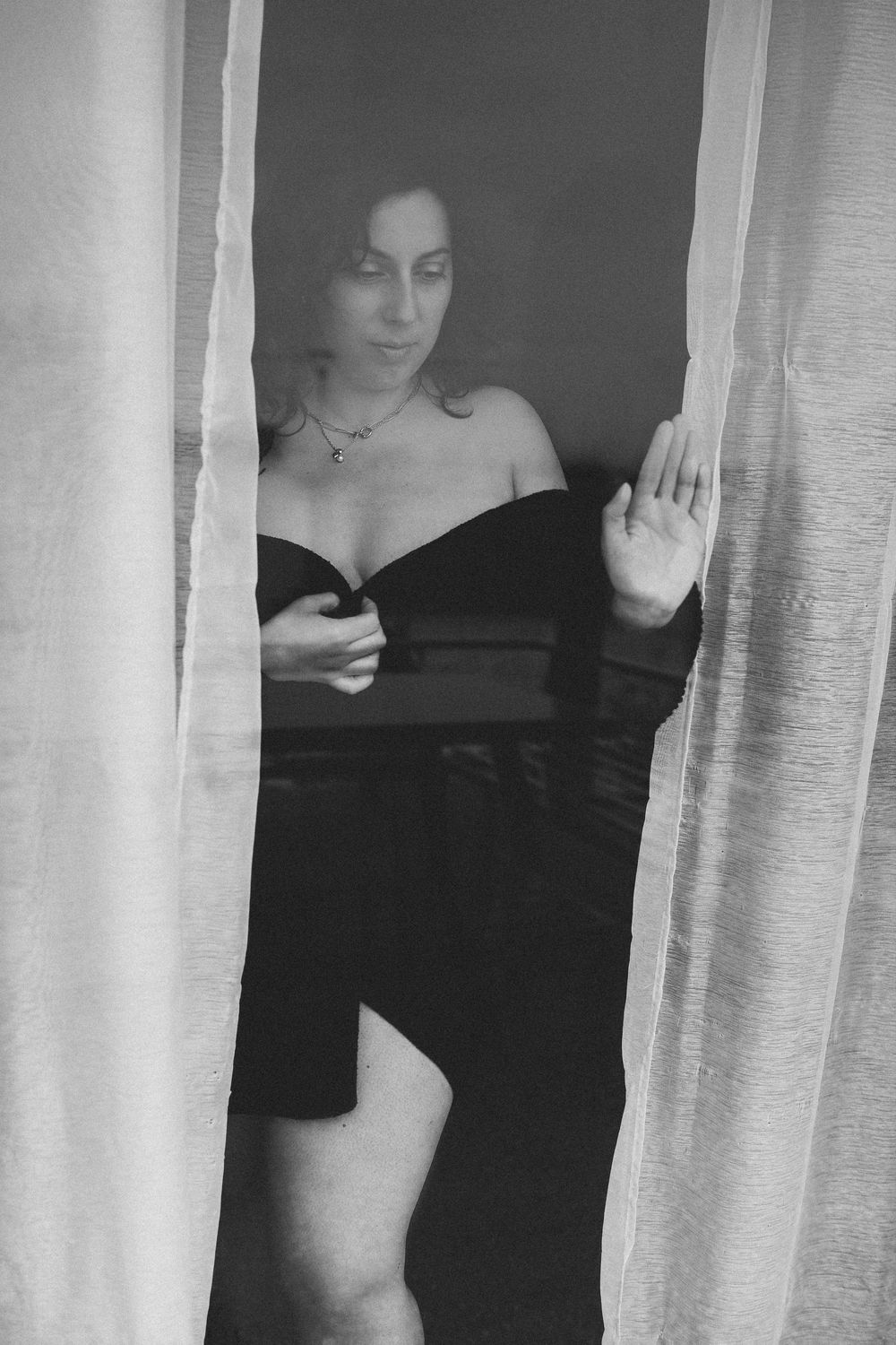 A black and white artistic photograph showing a figure behind sheer white curtains creating a mysterious atmosphere.