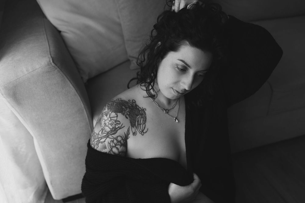 Black and white portrait showing shoulder tattoo and dark curly hair against light colored furniture.