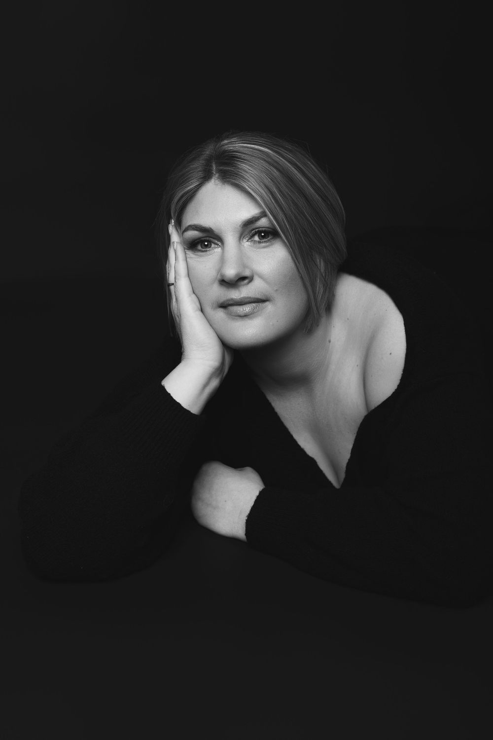 Black and white portrait of a woman resting her face on her hand against a dark background.