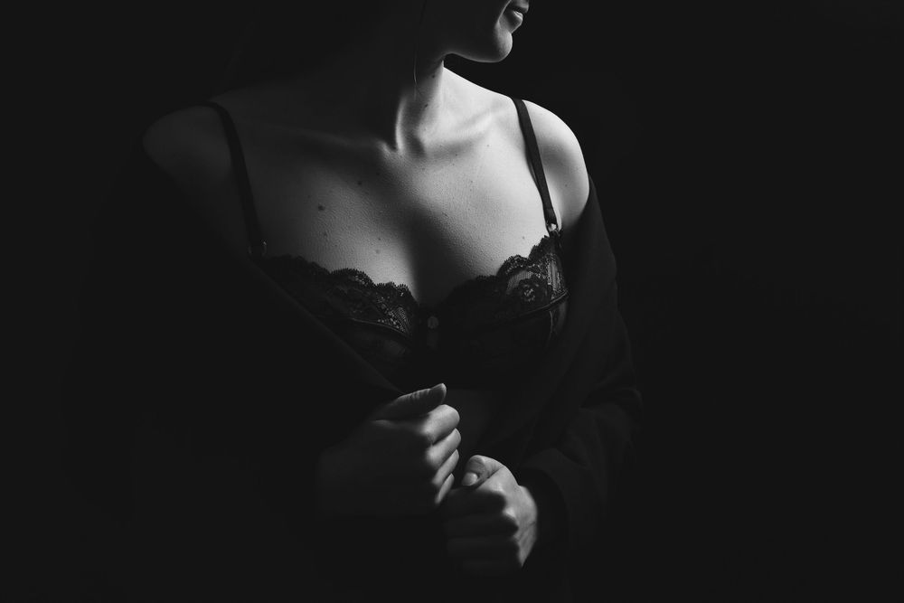 Black and white photograph of a person in dark attire looking down against a dark background.