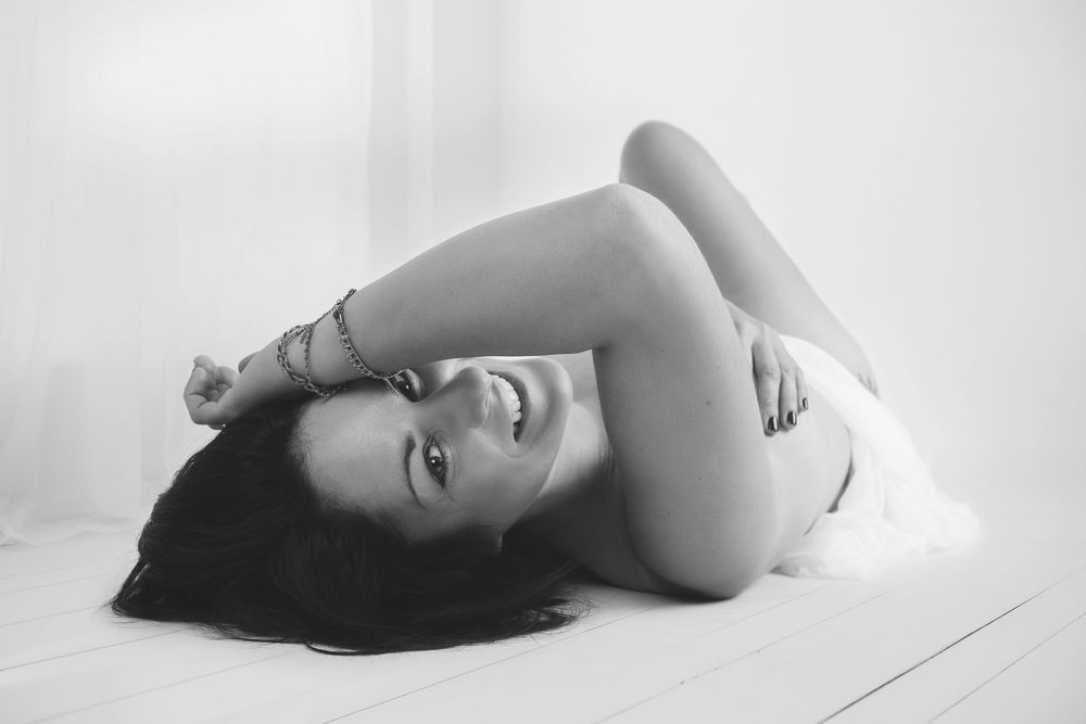 Black and white artistic nude photograph of a reclining figure against white background in minimalist style.