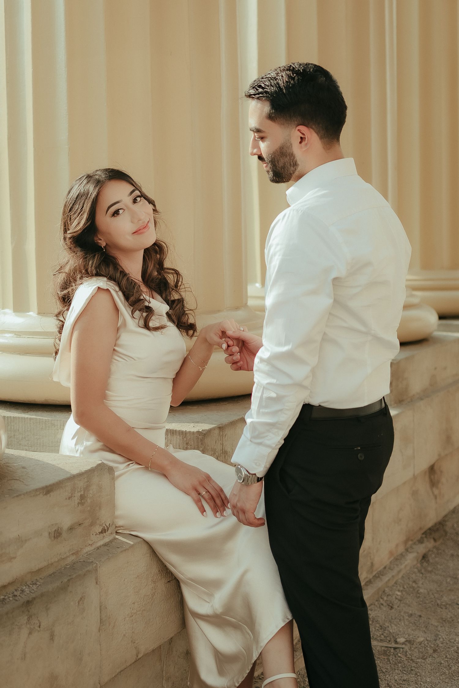 Elegant couple in formal wear sharing an intimate moment on classic stone architecture.