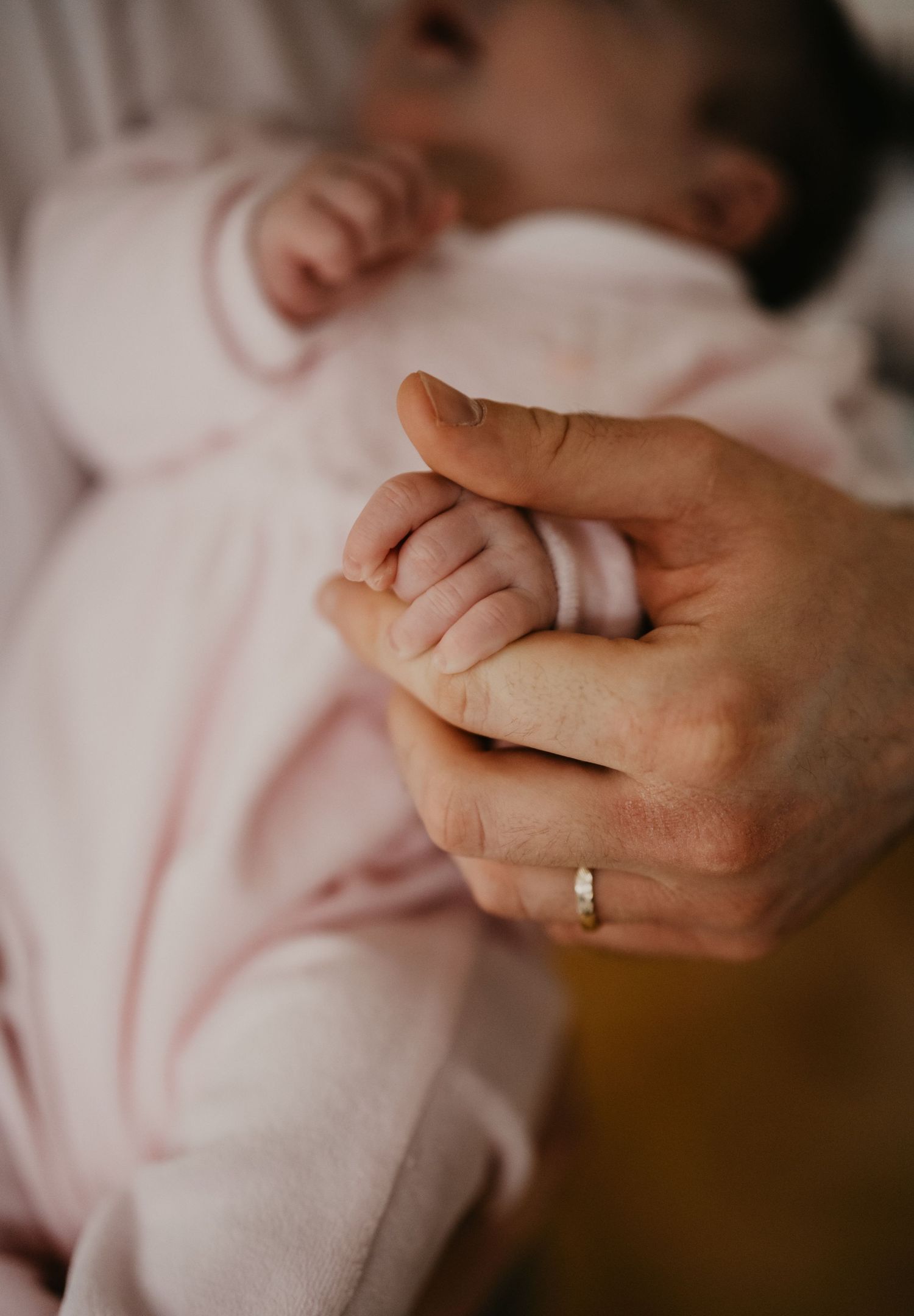 Close-up of an adult hand holding a baby's tiny hand while wearing a wedding ring.