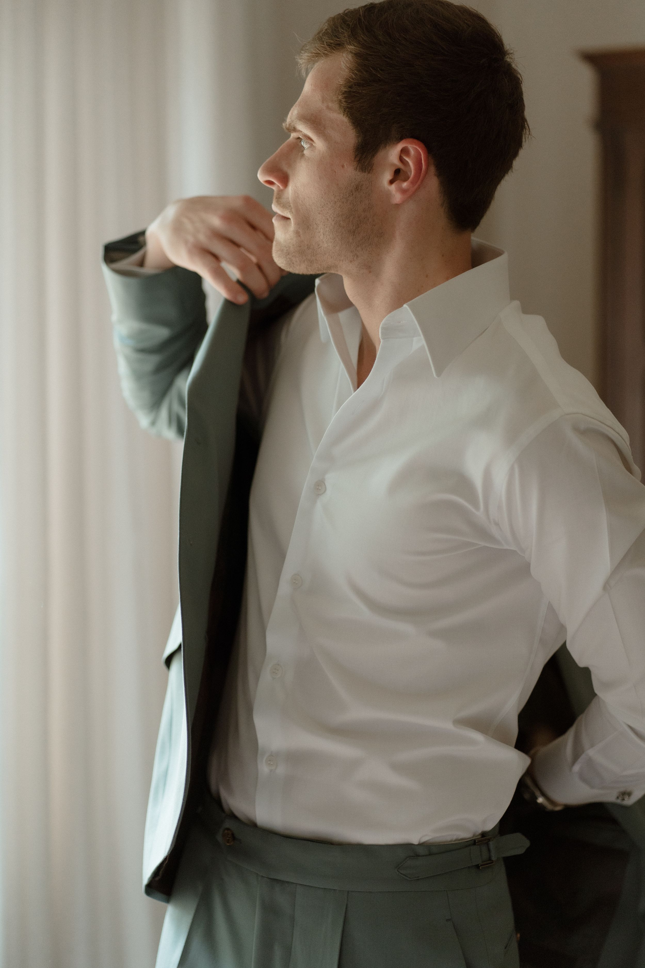 Side profile view wearing crisp white shirt and sage green suit jacket.