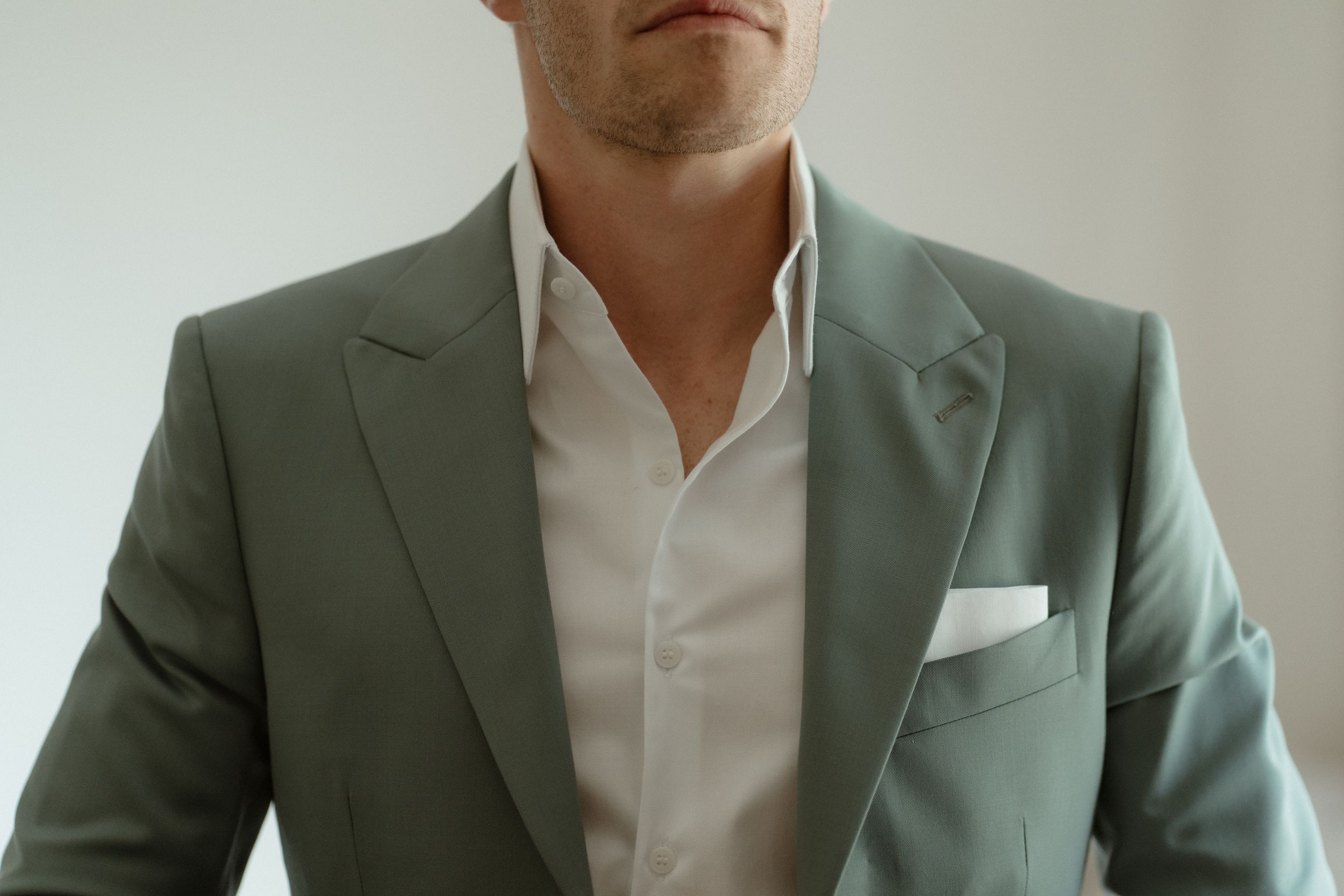 Close-up detail of sage green suit jacket with white dress shirt.