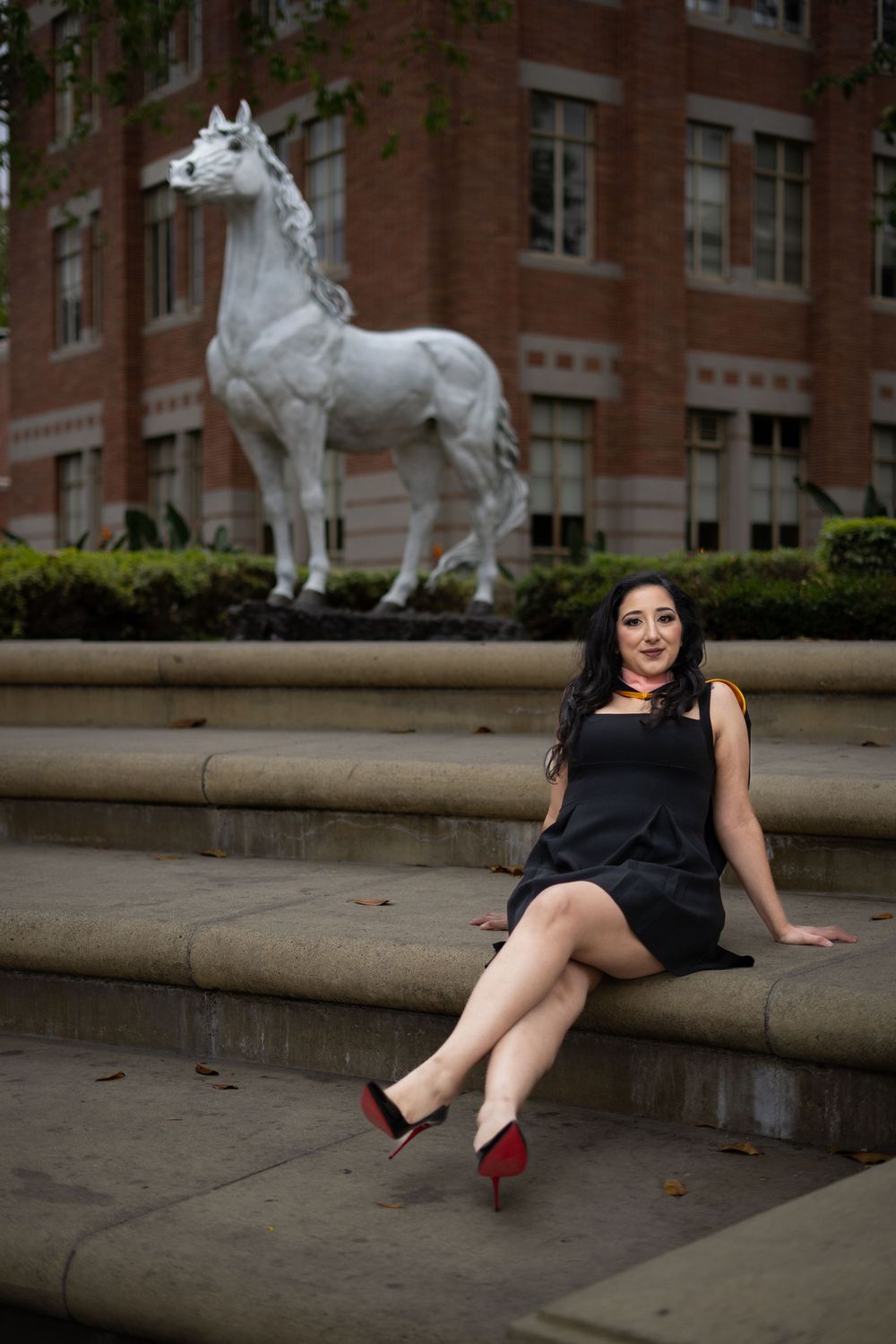 Graduate posing on stone steps with decorative horse statues in background.