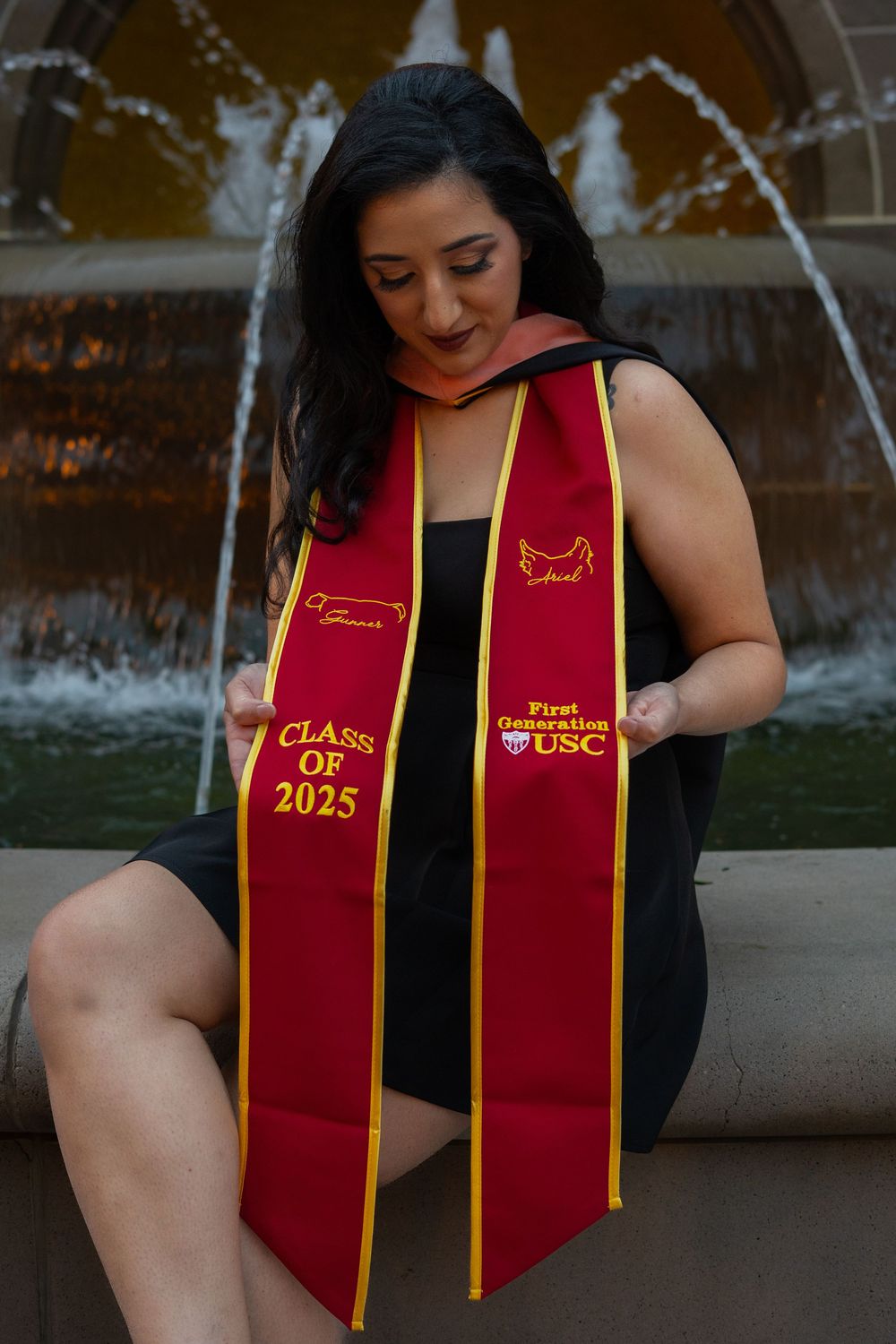 Graduate wearing Class of 2025 sash sits by fountain.