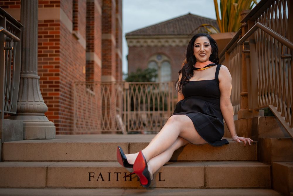 Graduate sitting on stone steps with engraved words.