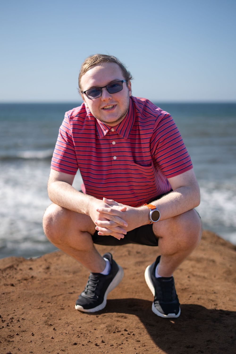 Person in pink striped shirt crouching on coastal bluff.