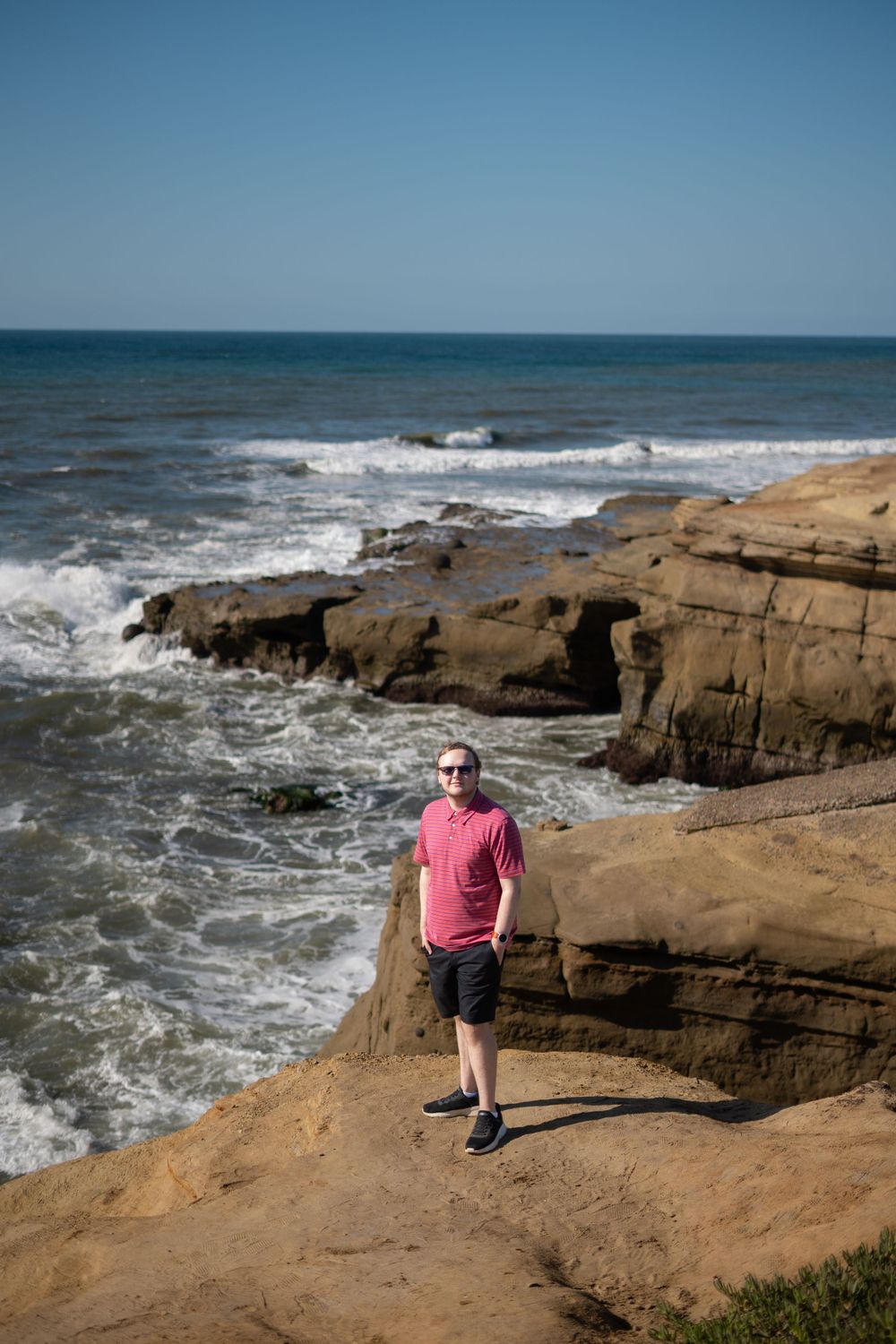 Person exploring rocky coastal cliffs by crashing ocean waves.