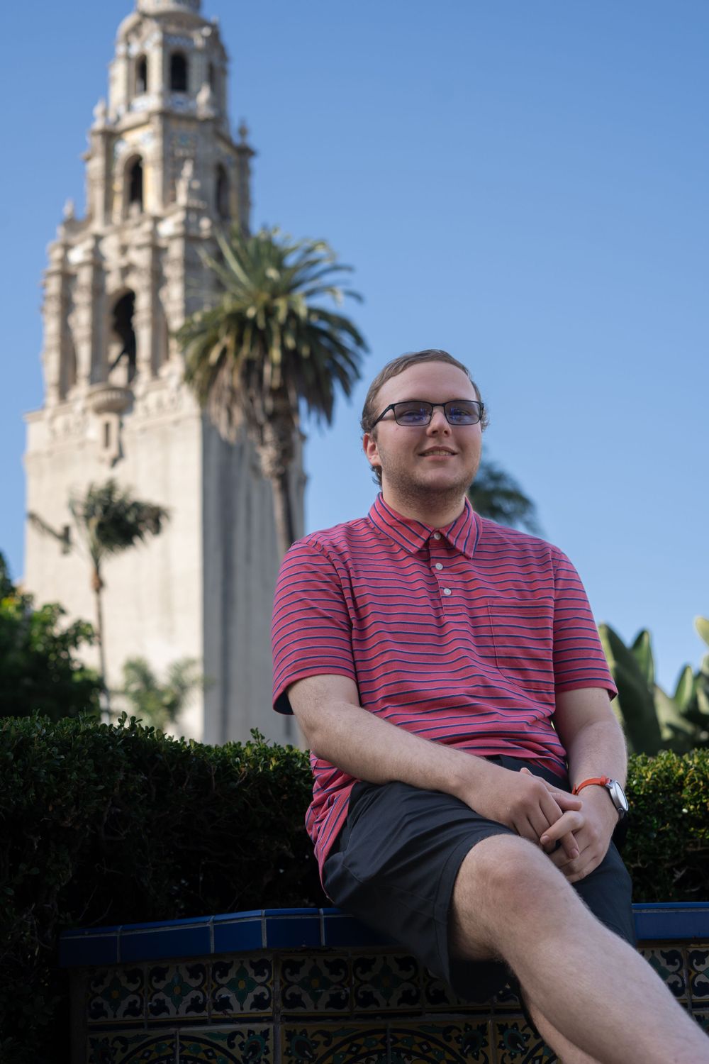 Person relaxing near historic Spanish-style bell tower under blue sky.