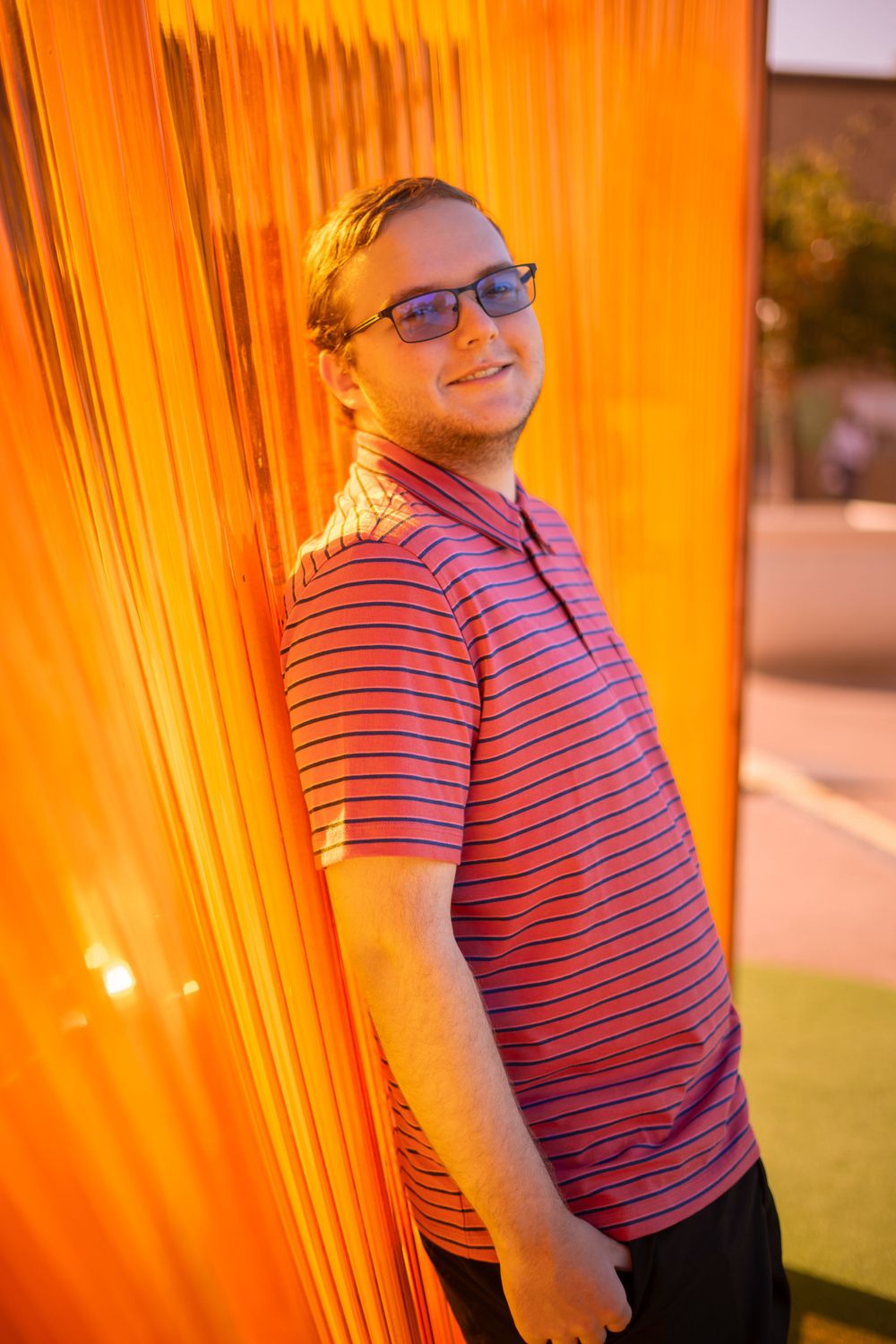 Person posing against orange-lit wall during golden hour.