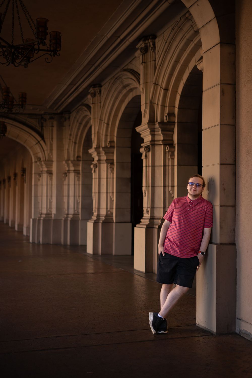 Person walking through arched colonnade hallway with dramatic lighting.