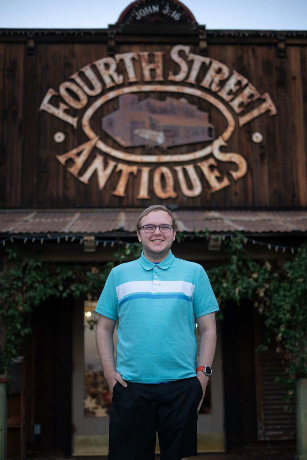 A person wearing a turquoise polo shirt stands in front of an antique store sign.