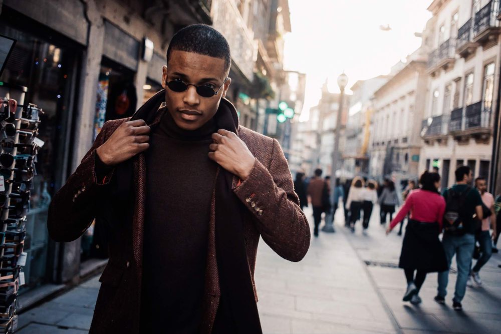 Stylishly dressed person in dark turtleneck and jacket walking on bustling European city street during daytime.