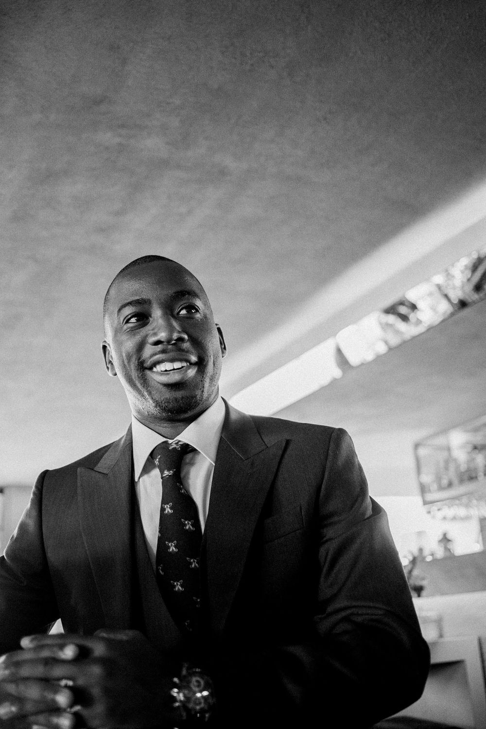 A professionally dressed businessman in a dark suit and tie smiles warmly in black and white photograph.