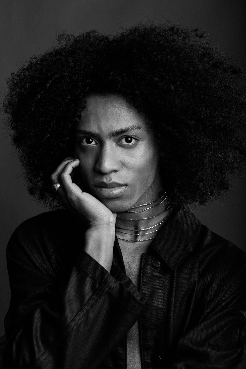 Black and white portrait of a person with natural curly afro hair wearing a dark top and metallic necklace.