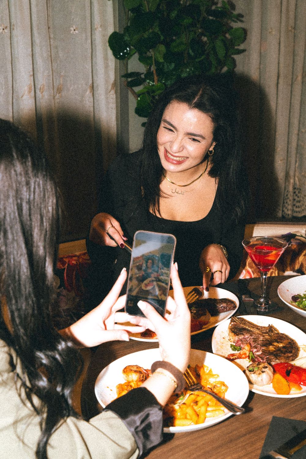 Friends sharing plates of food and drinks around a dinner table during an evening gathering at a restaurant.