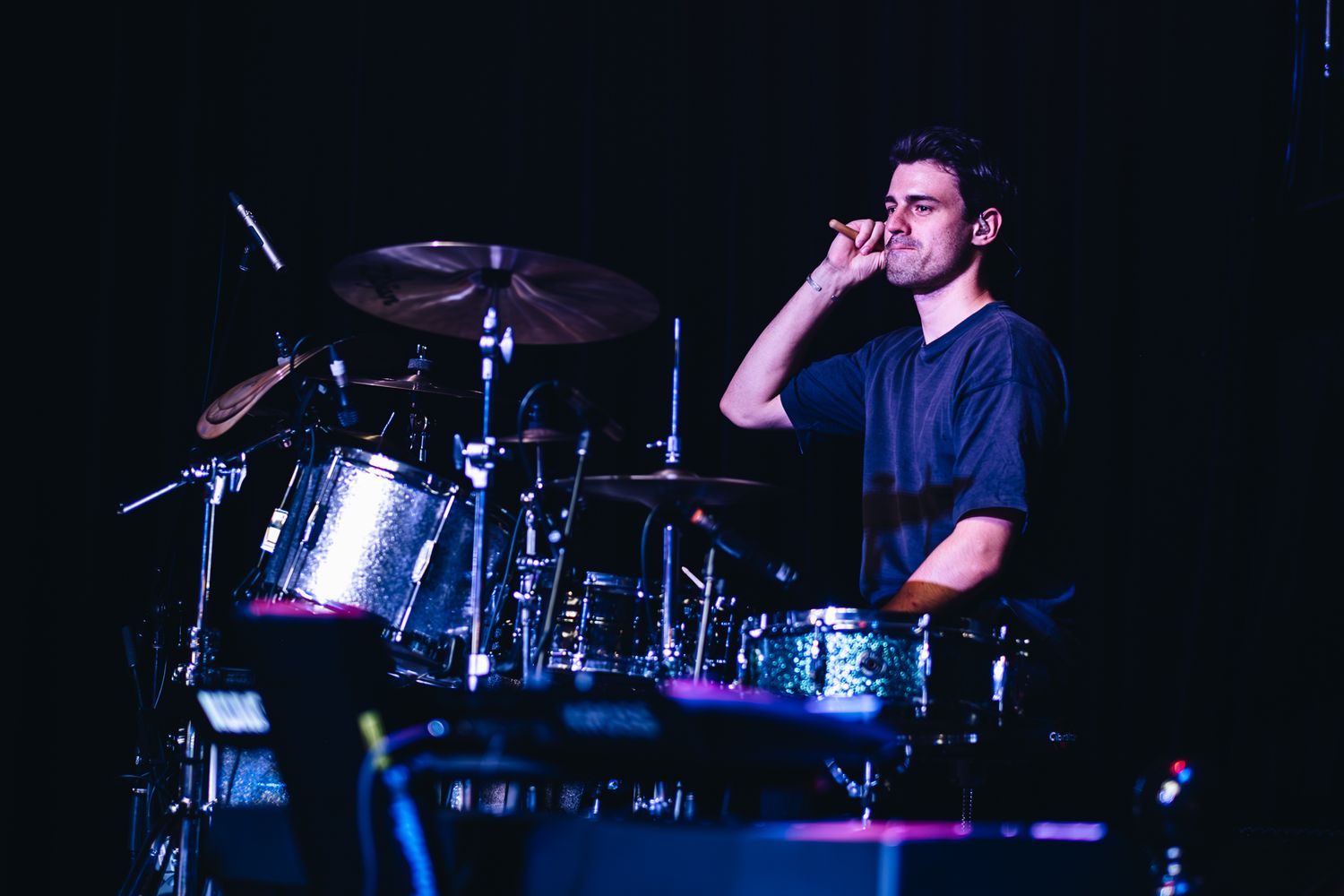 A drummer seated behind a drum kit on a dark stage during a live performance taken by a Melbourne concert and event photographer