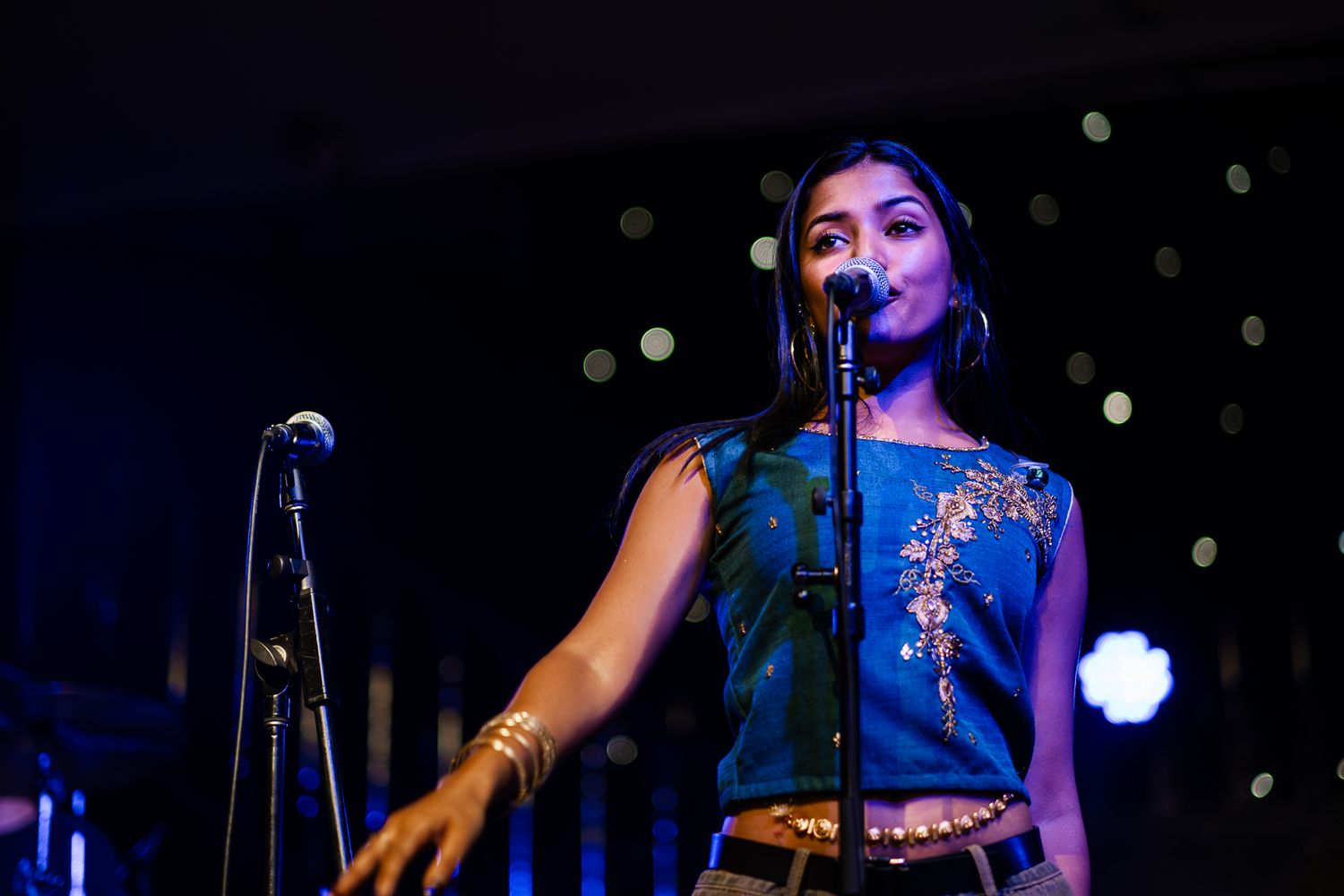 Concert performer in blue top singing into microphone on dark stage with bokeh lights in background taken by Melbourne concert  photographer