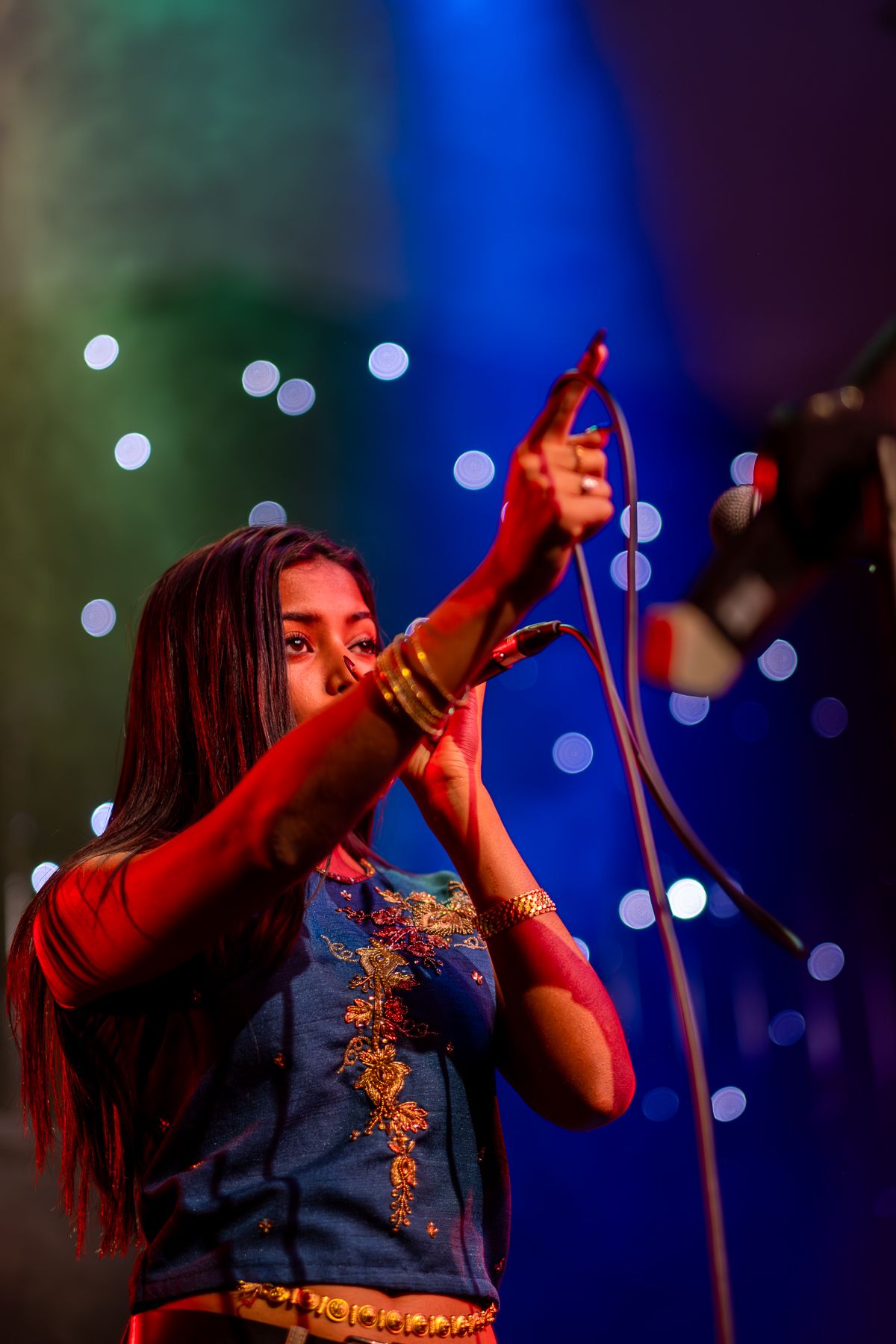 A performer in a blue tank top sings on stage during a concert performance taken by Melbourne concert photographer