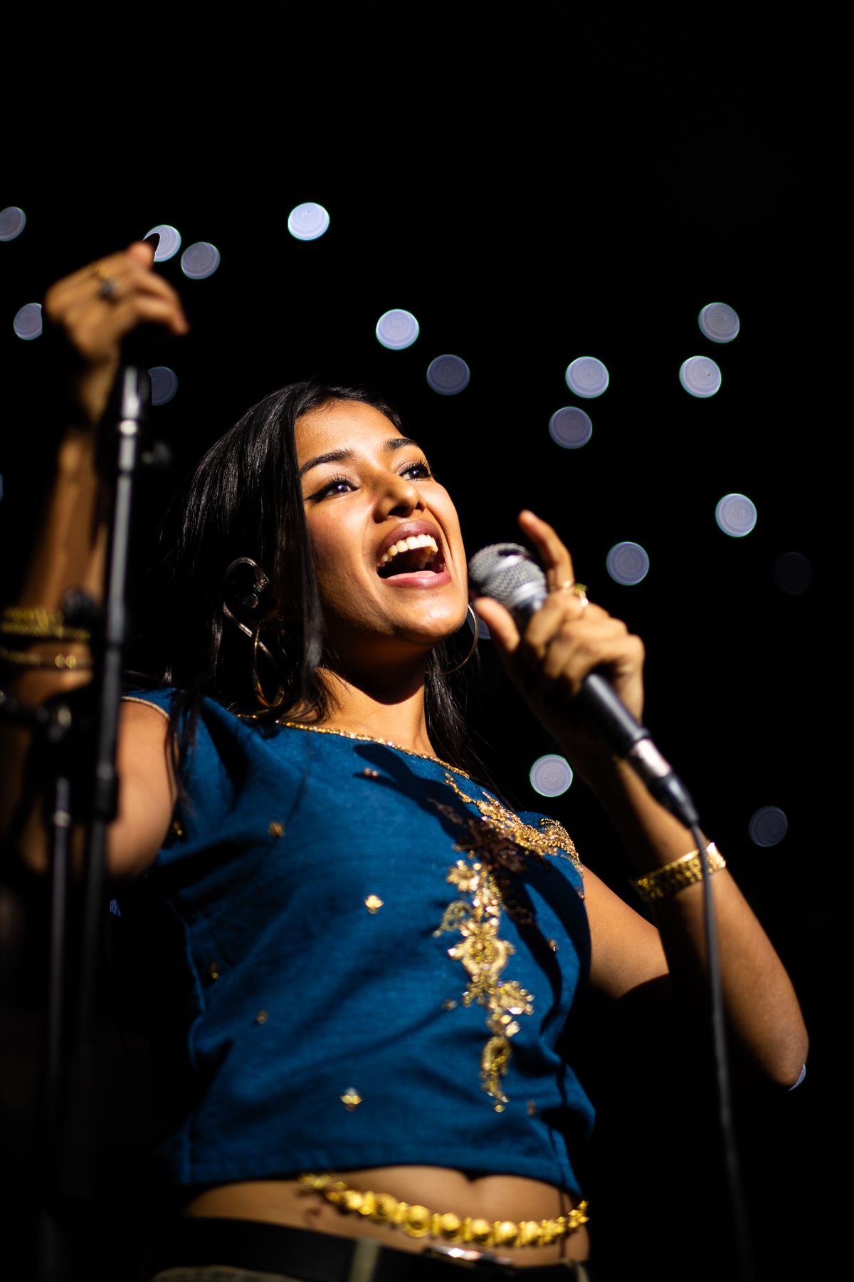A performer in a blue tank top sings on stage during a concert performance taken by Melbourne concert photographer