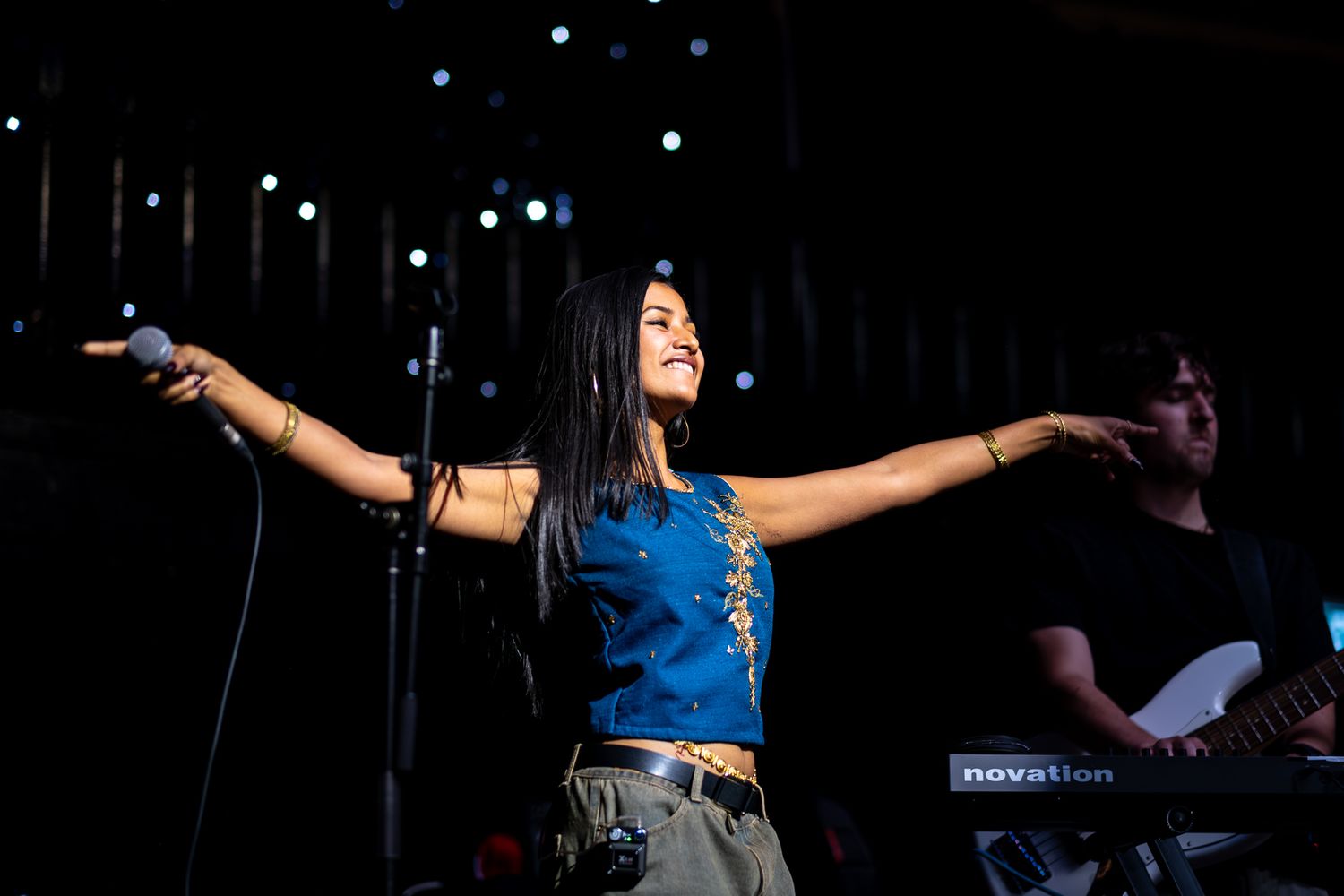 A performer in a blue tank top sings on stage with arms outstretched during a concert performance taken by Melbourne concert photographer