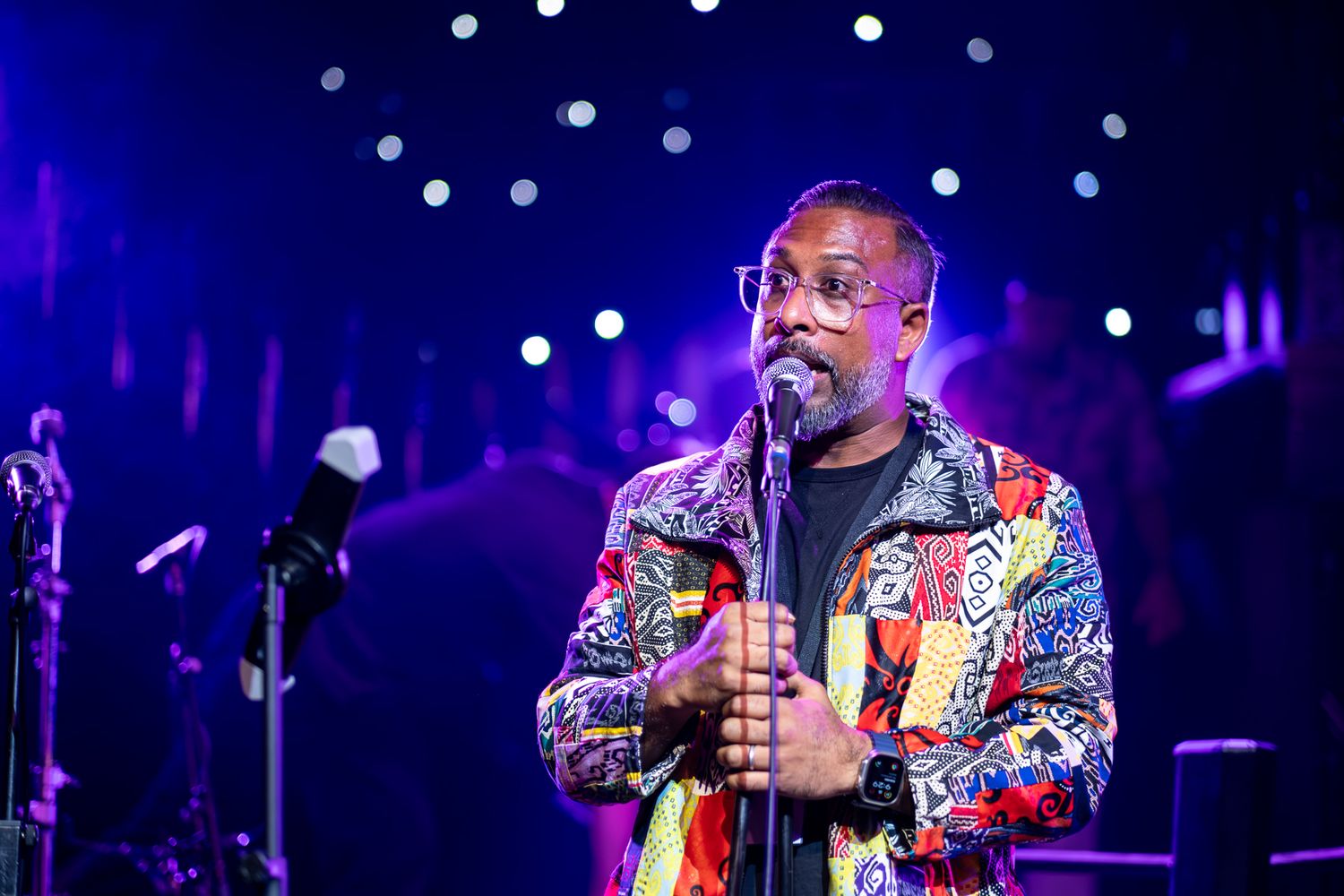 MC in colorful patterned jacket and glasses on stage with blue concert lighting in background taken by Melbourne event photographer