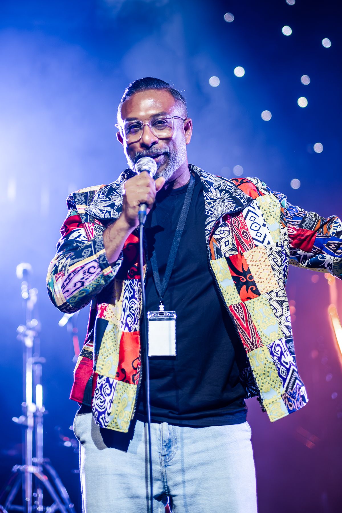MC in colorful patterned jacket and glasses on stage with blue concert lighting in background taken by Melbourne event photographer