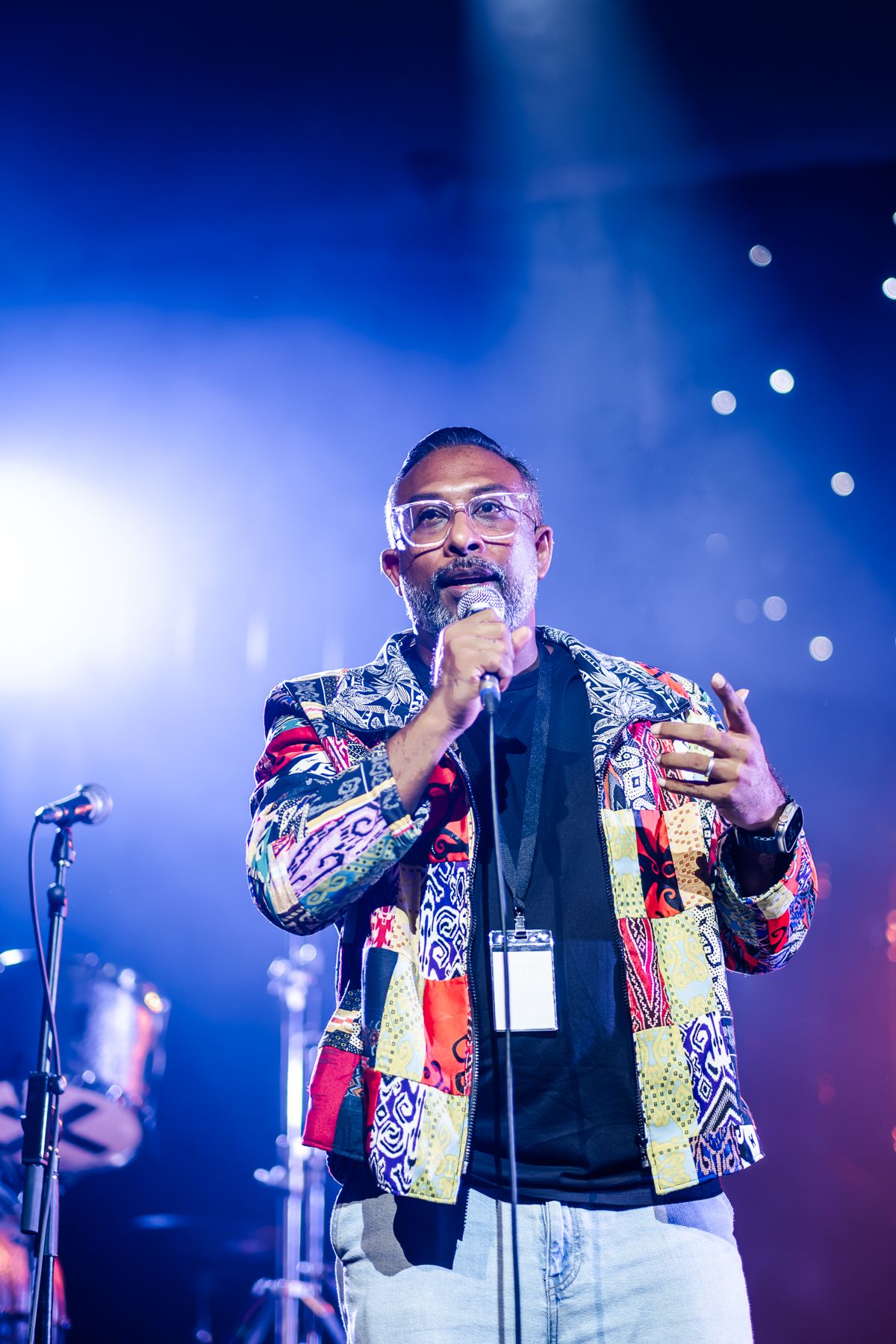 MC in colorful patterned jacket and glasses on stage with blue concert lighting in background taken by Melbourne event photographer