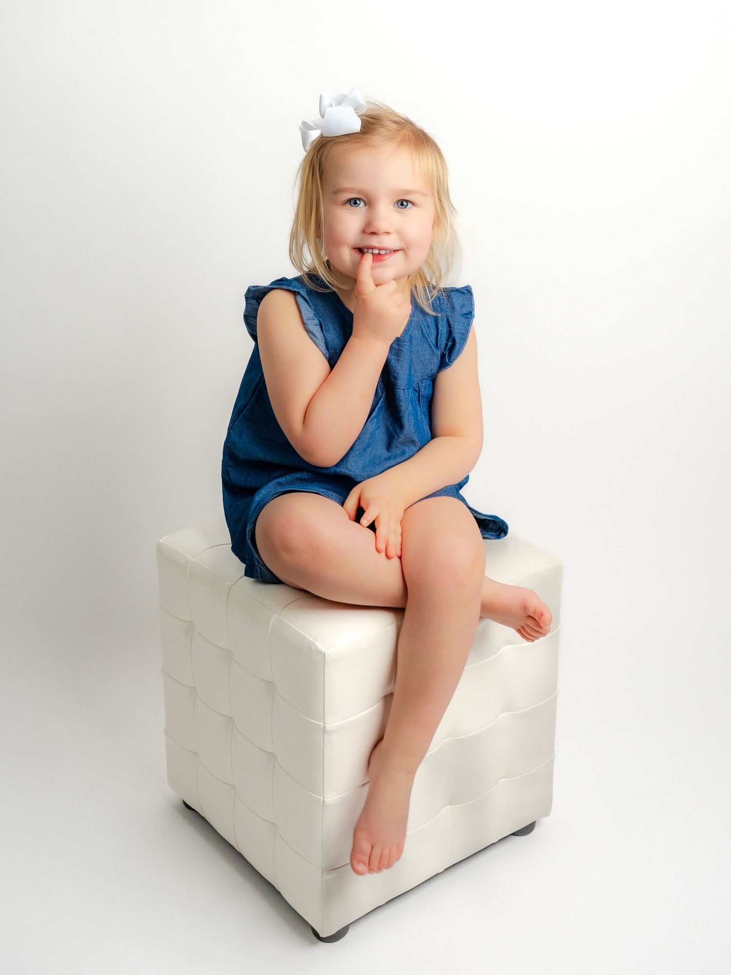 Photo of a little girl with a denim dress sitting on a white ottoman taken by Dandridge TN family portrait photographer
