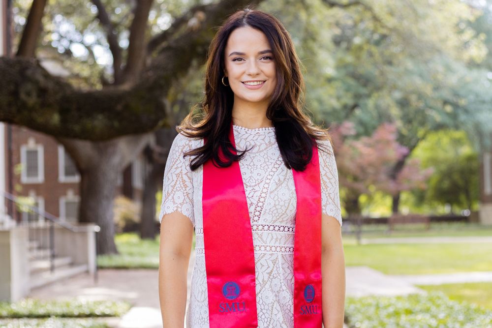 Professional headshot of person wearing red blouse against outdoor garden background.