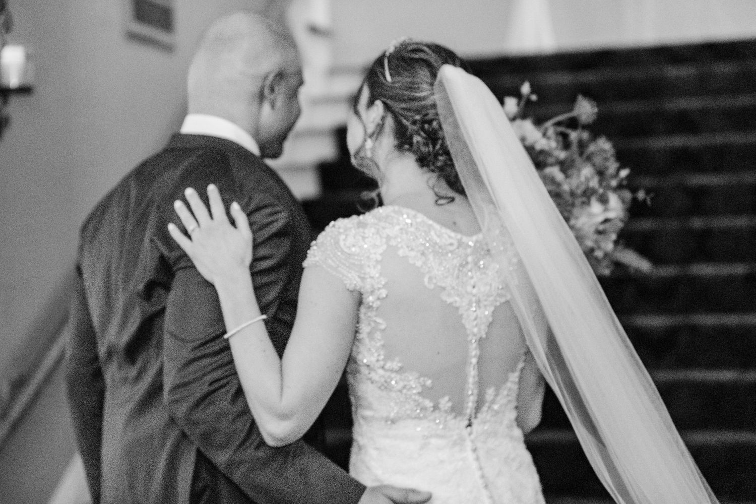 A black and white photo showing the intricate lace detail of a bride's wedding dress.