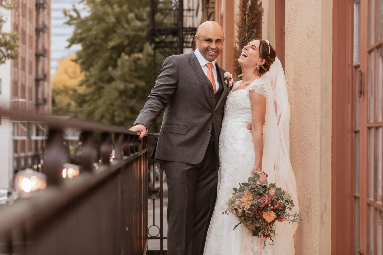 A couple shares a romantic moment on an urban balcony with fall foliage in the background.